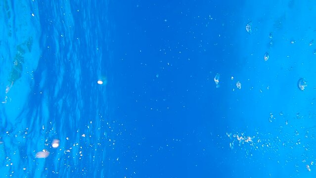 VERTICAL VIDEO: Slow motion of air bubbles floating to the water surface from sea bottom. Air bubbles up in the blue water on surface. Natural background, underwater shot