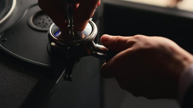Close up of male hands pressing freshly ground coffee in portafilter with tamper. Professional barista using modern tools for preparing tasty aroma coffee for clients.