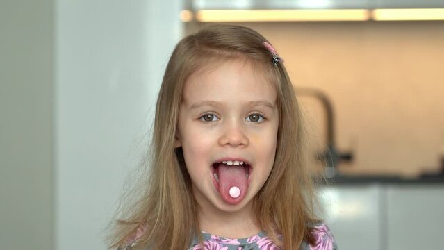 Happy little girl eats pill and fun stick out tongue with vitamin. Medicines, medicament and drug. Health, care and treatment for children.