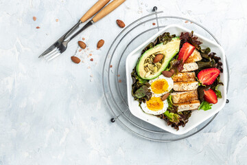 Ketogenic low carbs diet, Plate with keto foods: two eggs, avocado, grilled chicken fillet, nuts, strawberries and fresh salad. Healthy fats, clean eating for weight loss. top view