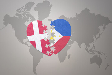 Fototapeta premium puzzle heart with the national flag of philippines and denmark on a world map background. Concept.
