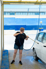 Adult woman with short hair cleaning a car with a pressure hose. Vertical image.