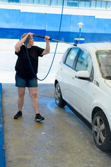 Adult woman with short hair cleaning a car with a pressure hose.