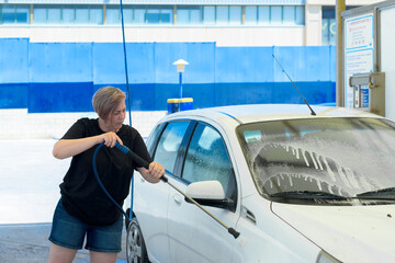 Horizontal medium shot image of an adult woman cleaning the windshield at a self-service car wash.