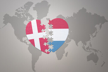 puzzle heart with the national flag of luxembourg and denmark on a world map background. Concept.