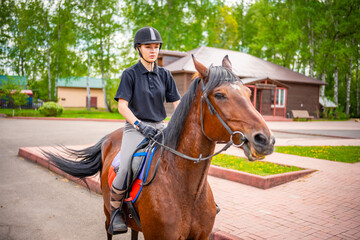 Lovely young woman wearing helmet riding her brown horse