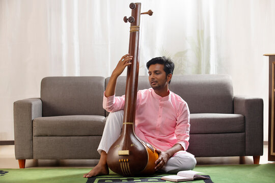 Young male classical singer playing Tanpura at home