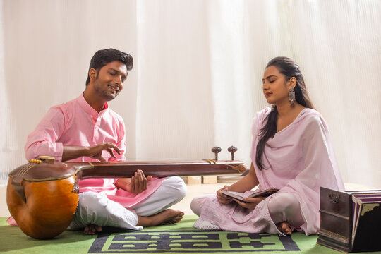 Young woman learning to play Tanpura with her music teacher at home