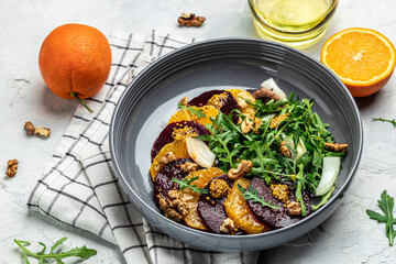 Arugula, Beet and oranges salad with walnuts on plate with fork, dressing and spices on gray background, Vitamin salad. Proper nutrition. place for text, top view