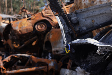 bracelet as symbol of ukraine - flag from blue and yellow with burnt out cars on background from russian attack. russian military war crimes against ukraine. glory to ukraine
