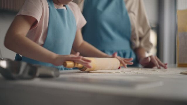culinary master class for children, little girl is rolling out dough for pie or bread in kitchen, closeup view