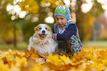 Friends, baby and dog are sitting together in beautiful golden leaves. Autumn in the park