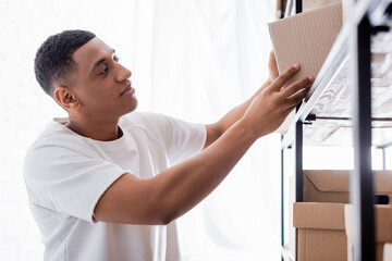 African american seller holding carton box near rack in online web store.