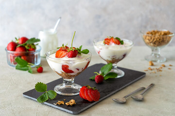 Yogurt with strawberry compote and granola, with fresh fruits, mint in dessert cups on slate board. Grey background