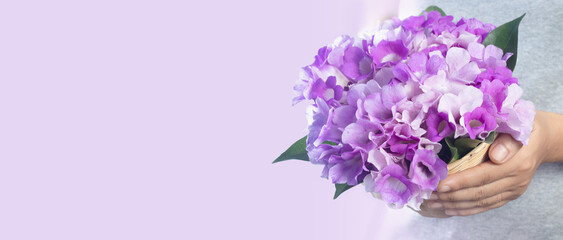 hand holding a basket of fresh purple flowers isolated on a pastel pink background with free space for text