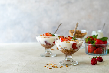 Yogurt with strawberry compote and granola, with fresh fruits in dessert cups on grey background....