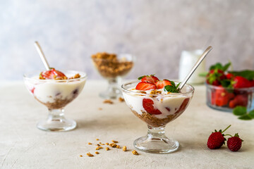 Yogurt with strawberry compote and granola, with fresh fruits in dessert cups on grey background