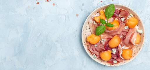Summer appetizer with sweet melon and prosciutto and basil. Antipasti, Traditional Spanish and Italian appetizer. Top view on white stone table, Long banner format. top view