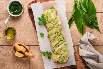 Braided wild garlic pesto brioche. Homemade raw or uncooked fresh pull apart bread with wild garlic pesto on wooden board on old beige tiles background. Italian bread. Copy space. Top view.
