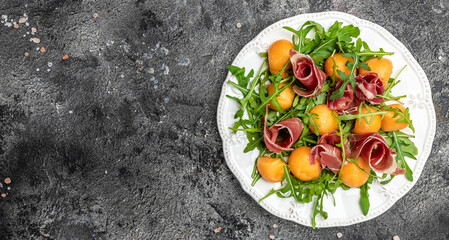 Fresh melon with prosciutto and basil. Antipasti, Traditional Spanish and Italian appetizer. Top view on dark stone table, Long banner format. top view
