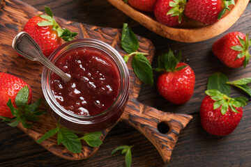 Strawberry jam. Strawberry jam in glass jar with fresh berries plate on an old wooden dark table background, closeup. Homemade strawberry fruity jam. Top view with copy space.
