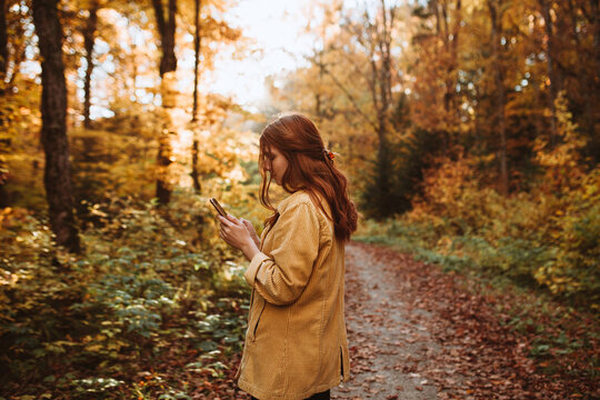Woman standing browsing on mobile phone in autumn forest