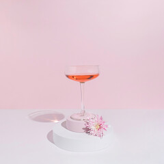 Minimal pastel party concept with bright pink flower and wine glass. Modern spring or summer aesthetic.