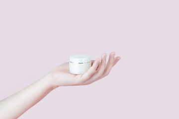 Skin care for healthy skin. Woman hand holding moisturizing​ cream bottle isolated on pink background. Beauty​ and cosmetic concept.