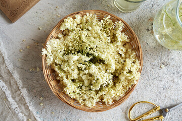 Fresh elder flowers in a basket with a jug of lemonade with elder flower syrup