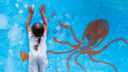 Unidentified little girl is messy painting the wall of ocean world and sea animals, and paint hand...