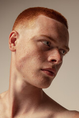 Close-up portrait of handsome young red-haired man with freckles posing isolated over grey studio...