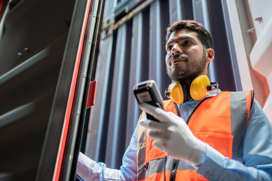 Dock worker man in safety vest holding barcode scanner and inspector the quality of container at shipping yard. Import and export product. Manufacturing transportation and global business concept