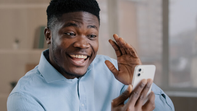 Happy young african american guy businessman handsome entrepreneur man worker hold smartphone talk by video call greeting have virtual meeting chat with friend distance communication remote conference