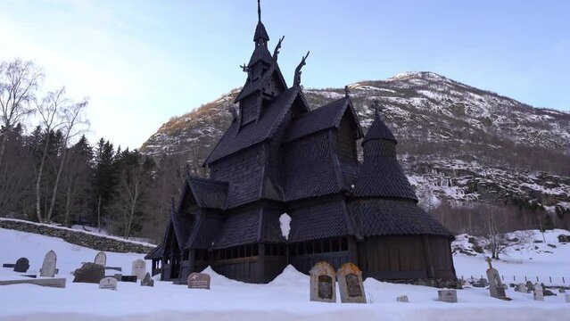 Ancient Borgund Stave church during winter with mountain background - Walking sideways with church in center of frame - Norway wide angle