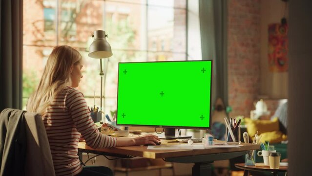 Concentrated Female Designer Working From Home at Desktop Computer with Green Screen. Woman Using Computer Mouse while Thinking About New Project. Freelance and Millennial People Concept