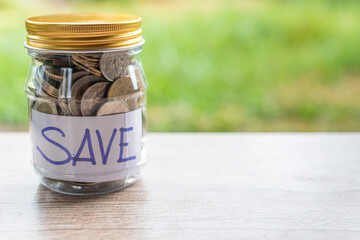 Coins and text SAVE in a glass jar placed on a wooden table. Concept of saving money for investment and emergency situations. Close up, Blurred background