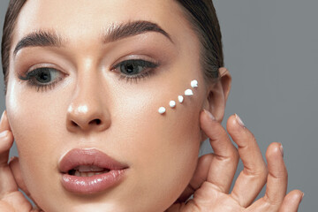 Beauty Face. Beautiful Woman With Natural Makeup Applying Cream To Her Face . Closeup Portrait Of Model Girl With Healthy Smooth Facial Skin.