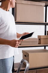 Cropped view of african american seller holding digital tablet near cardboard boxes in online web store.