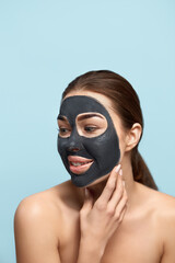 Beautiful young woman with mask for the face of black clay on clean fresh skin . Girl model beauty face care with  cosmetic mask  touches her face . Facial treatment . Skin care