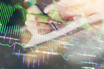 Financial forex graph displayed on hands taking notes background. Concept of research. Double exposure