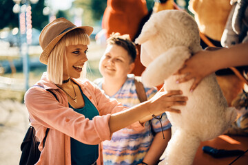 Happy woman gets stuffed toy at carnival both after winning in shooting game at amusement park.