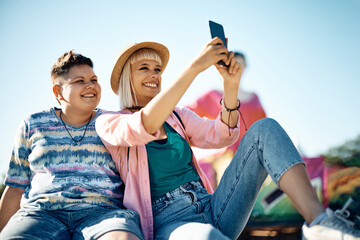 Happy female friends taking selfie while having fun at amusement park.