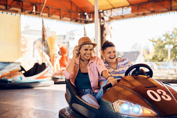 Carefree lesbian couple has fun while driving bumper car at amusement park.