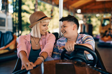Obraz na płótnie Canvas Happy lesbian couple talks while driving bumper car at amusement park.