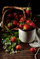a berry falls into a cup with strawberries, a basket with berries and a bouquet of forest flowers in the background