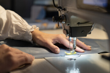 Woman tailor work on sewing machine stitching patterns of new collection. Closeup shot of female sewer hand dressmaking. Seamstress use professional equipment for tailoring. Garment industry concept