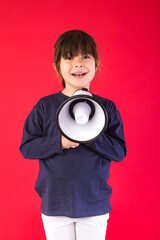 Black-haired girl in a blue sweater and white pants, speaking through a white megaphone, on a red background.