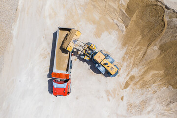 Aerial view of sand quarry with trucks and bulldozers. Heavy bulldozer loading sand. Aerial view of sand quarry with bulldozer.  - obrazy, fototapety, plakaty