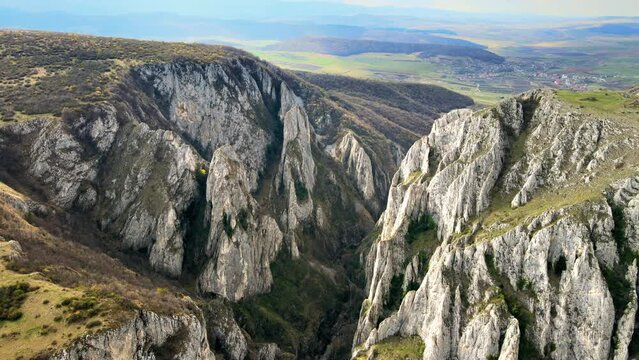 Aerial drone view of a rocky canyon in Romania. Rocky cliffs with sparce vegetation. Fields in the distance