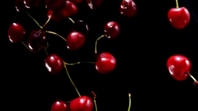 Delicious juicy red cherries are falling diagonally on a black background
